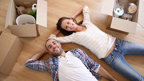 house with a for sale sign two people lying on the floor with boxes